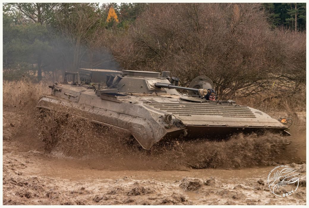 Bojové vozidlo pěchoty projíždí řídkým blátem na vojenském cvičišti.
